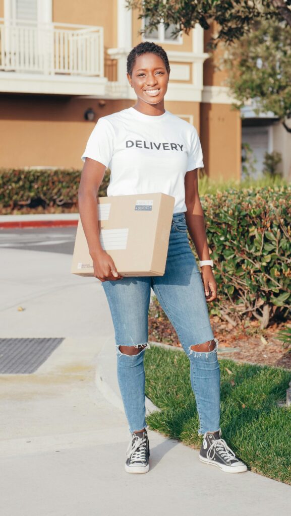 African American delivery woman smiling while holding a package outdoors during day.